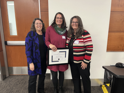 three people stand together holding an award and smiling for the camera